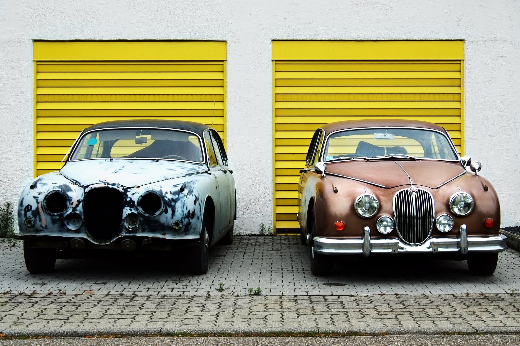 Old run down car next to well maintained car both in front of yellow garage doors